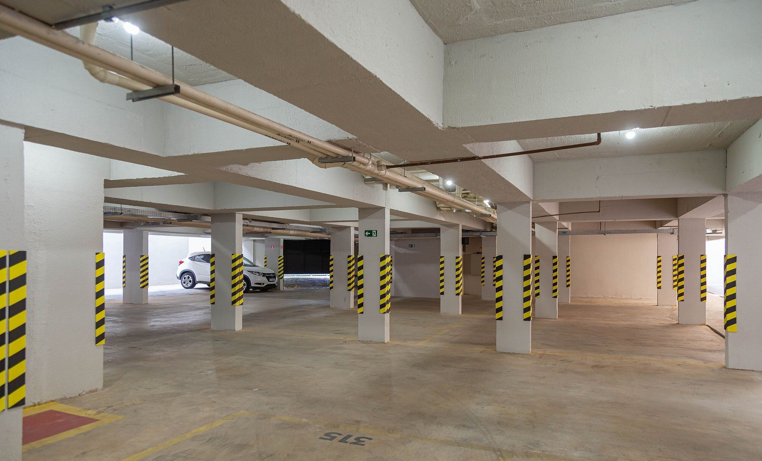 An indoor parking garage with concrete pillars, yellow and black striped barriers, and a white car parked in the distance.