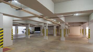 An indoor parking garage with concrete pillars, yellow and black striped barriers, and a white car parked in the distance.