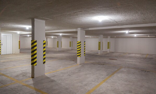 A parking garage with concrete pillars and yellow stripes, concrete floor with parking lines, and a white door. - Charming Studio in Pocos de Caldas-mg Pgo209 (Poços de Caldas)