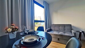 Ein Essbereich mit Tisch für zwei Personen, einer Couch und einem Fenster mit Vorhängen.