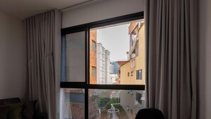 A hotel room with a large window, a dining table with a chair, and a sofa. - Studio w/ Swimming Pool in Pocos de Caldas Pgo0406 (Poços de Caldas)
