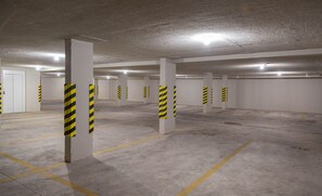 Un parking avec des piliers en béton et des bandes jaunes, un sol en béton avec des marquages au sol indiquant les places de stationnement, et une porte blanche.