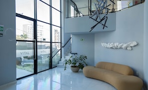 Un hall d’entrée moderne avec une entrée en verre, un escalier, une plante en pot et un canapé beige.