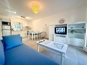 A modern living room with a sofa, a TV, a dining area, and a kitchen. - Apartment 'Addaia' with Mountain Views, Shared Pool and Wi-Fi (Port d'Addaia)