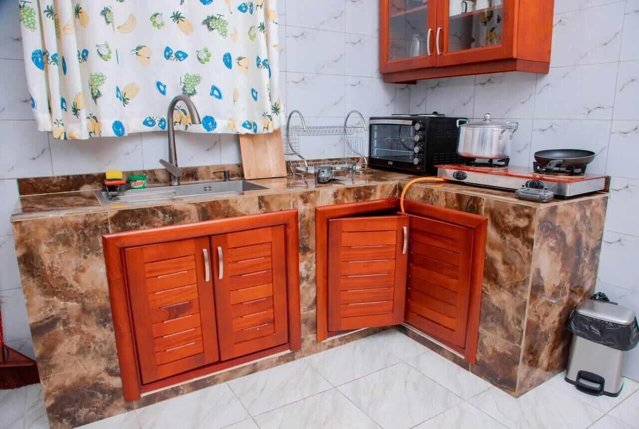 A kitchen with a marble countertop, wooden cabinets, a microwave, a stove, and a trash bin.