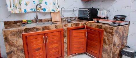 A kitchen with a marble countertop, wooden cabinets, a microwave, a stove, and a trash bin.