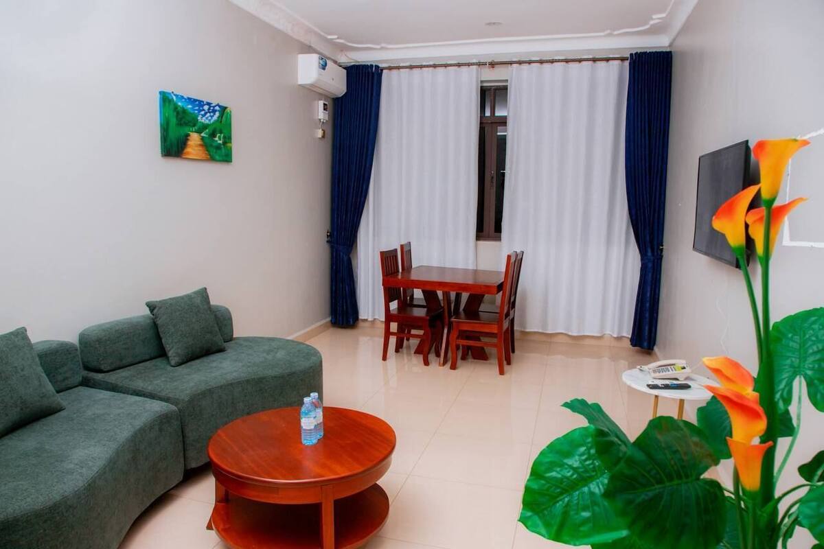 A living room with a sofa, a dining table with chairs, a small round table with a bottle, and a painting on the wall.