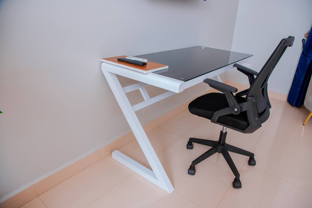 A modern office desk with a glass top, black office chair, and a white frame.