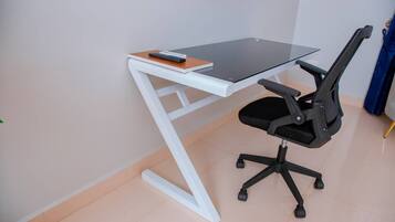 A modern office desk with a glass top, black office chair, and a white frame.