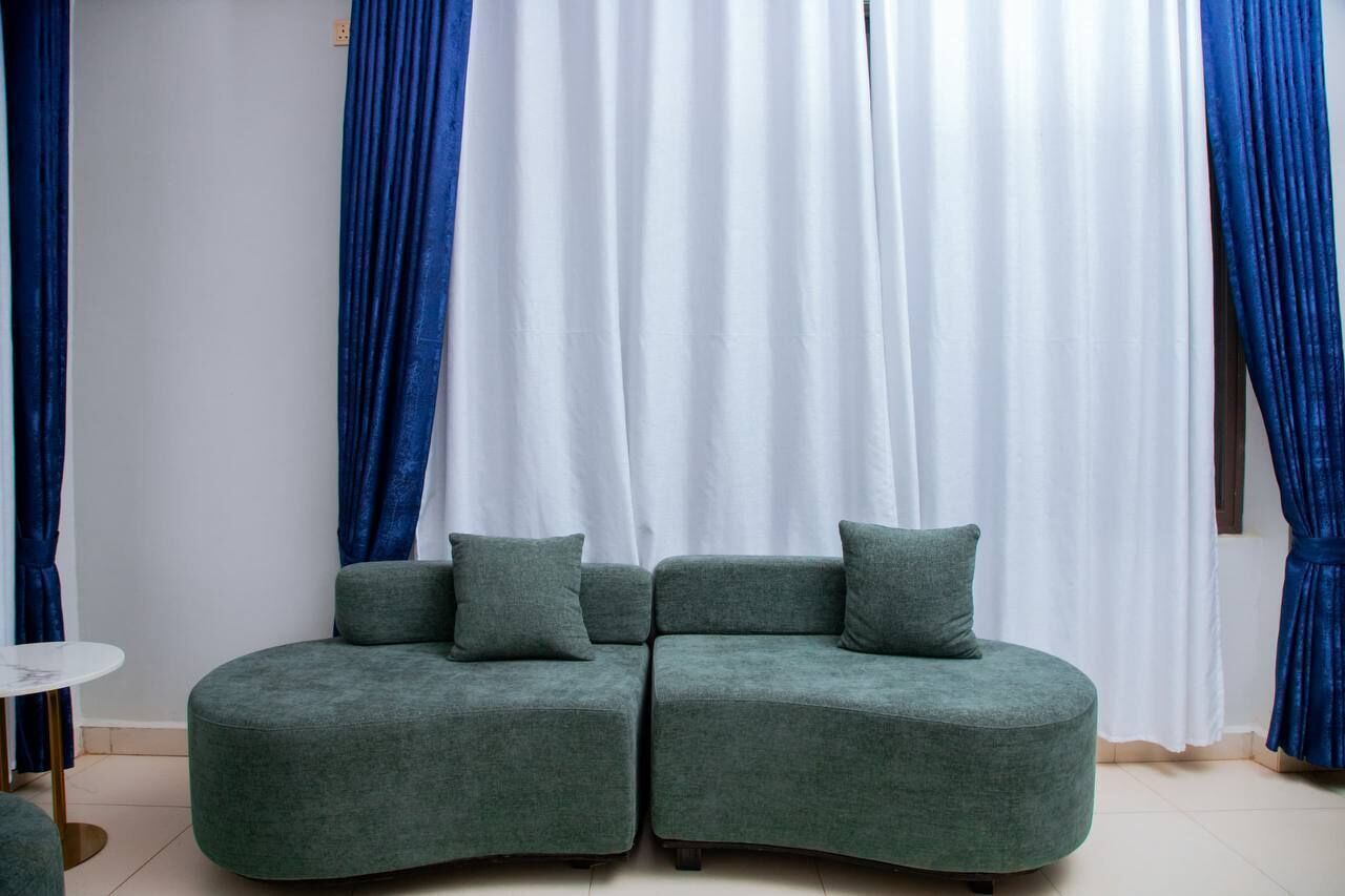 Une pièce avec un canapé d’angle vert, une petite table ronde et des rideaux bleus.