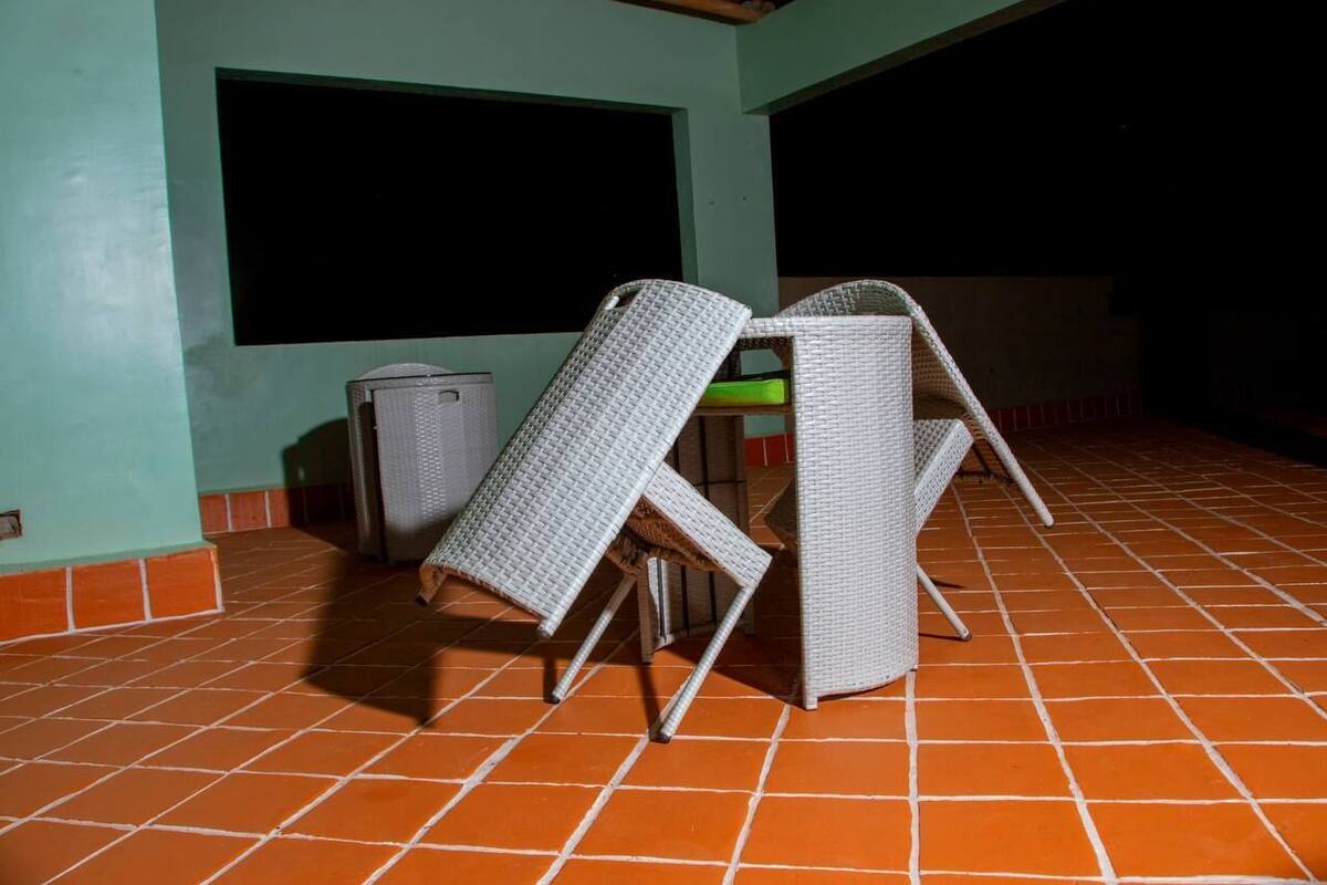 A room with a tiled floor, two white wicker chairs, a small table, and a trash bin.