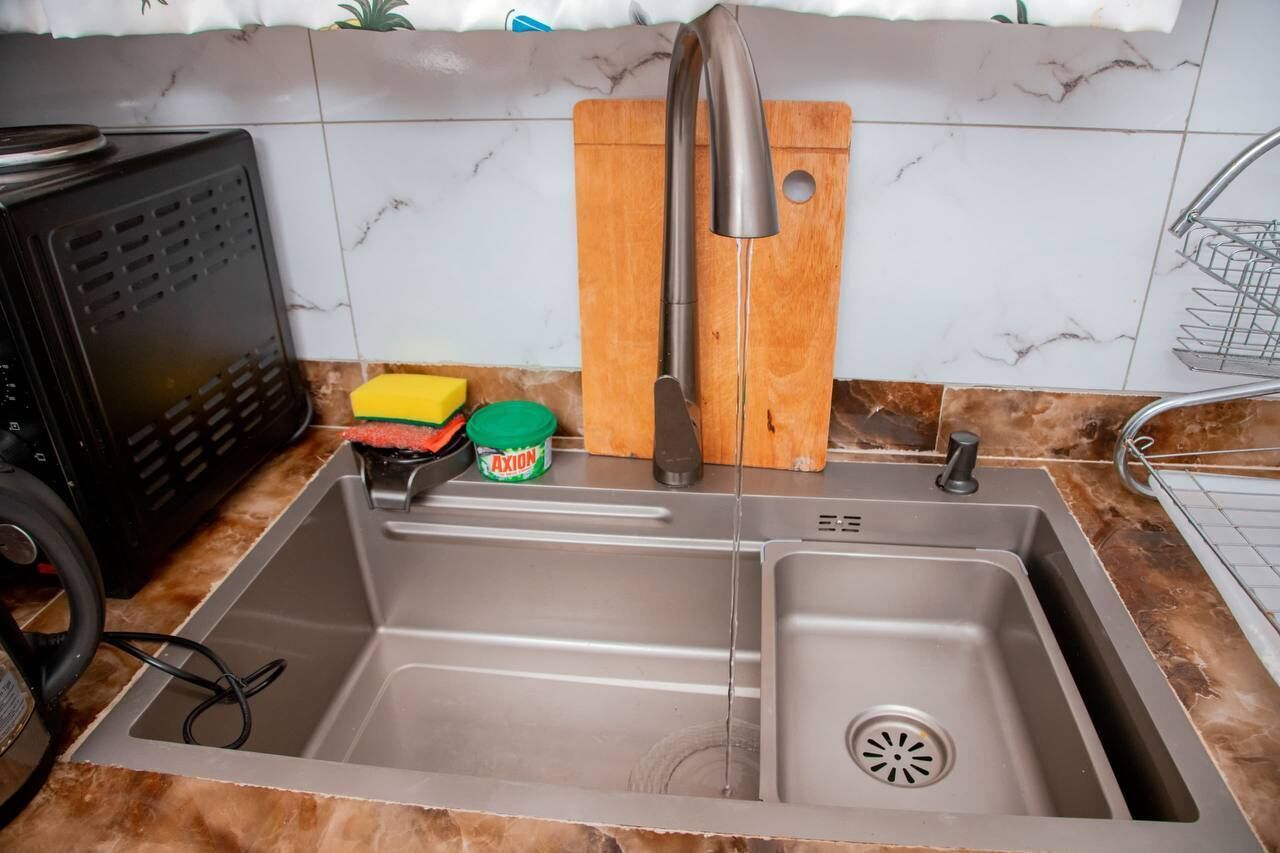 A kitchen with a double sink, a wooden cutting board, a knife, a sponge, and a container of AXION detergent.