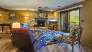 A living room with a stone fireplace, a ceiling fan, a television, and a view of the outdoors. - Affordable stay with gorgeous views! (Gatlinburg)
