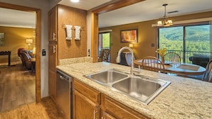 A kitchen with granite countertops, stainless steel sink, wooden cabinets, and a dining area with a table and chairs. - Affordable stay with gorgeous views! (Gatlinburg)