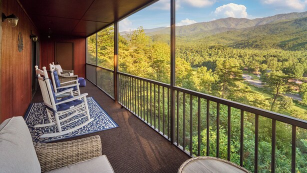 A balcony with wicker furniture and a patterned rug, overlooking a forested valley with mountains in the distance. - Affordable stay with gorgeous views! (Gatlinburg)