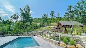 A swimming pool with a wooden deck, surrounded by a stone wall and a fence. - Affordable stay with gorgeous views! (Gatlinburg)