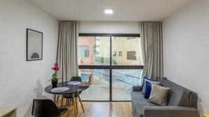 A modern living room with a grey sofa, a dining table with chairs, and a large window with curtains.