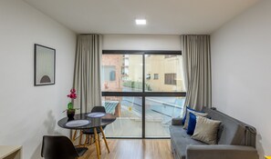 Una sala de estar moderna con un sofá gris, una mesa de comedor con sillas y un amplio ventanal con cortinas.