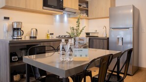 Une cuisine moderne avec des meubles en bois, un réfrigérateur en acier inoxydable, un four à micro-ondes encastré, une machine à café et une table à manger avec des chaises.