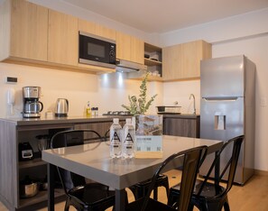 Une cuisine moderne avec des meubles en bois, un réfrigérateur en acier inoxydable, un four à micro-ondes encastré, une machine à café et une table à manger avec des chaises.
