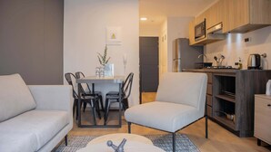 A modern living room with a sofa, a dining table with chairs, and a kitchen area with cabinets and appliances. - w Striking 1BR Duplex in Miraflores (Lima)