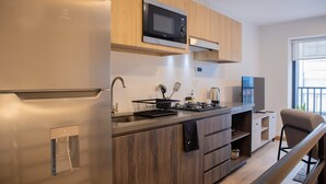 A modern kitchen with a built-in microwave, a stainless steel refrigerator, wooden cabinets, and a small dining area with a chair. - w Striking 1BR Duplex in Miraflores (Lima)