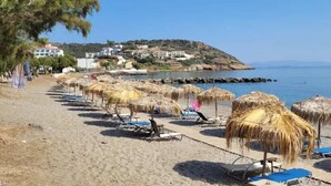 A beach with thatched umbrellas, lounge chairs, and a clear view of the sea. - Beachfront Ela Luxury Stay With Jacuzzi Views (Kithira)
