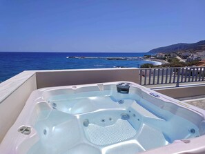 A hot tub on a balcony with a view of the sea and a pier.