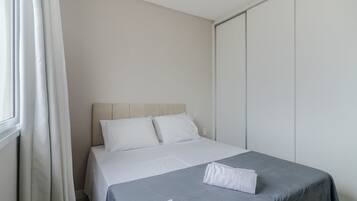 A bedroom with a bed, white curtains, and a grey bedspread.