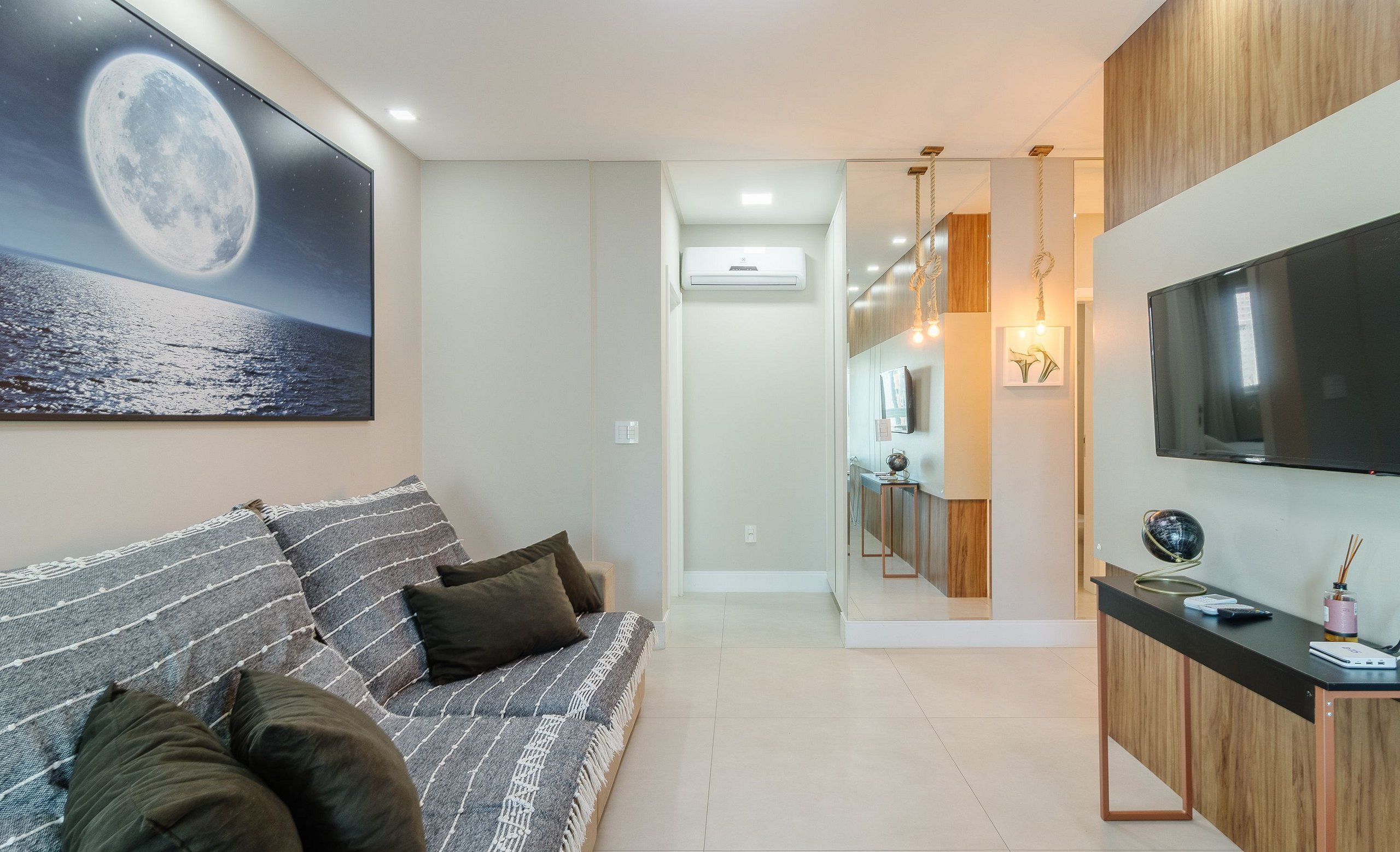 A modern living room with a large flat-screen TV, a sofa with cushions, and a painting of a moon on the wall.