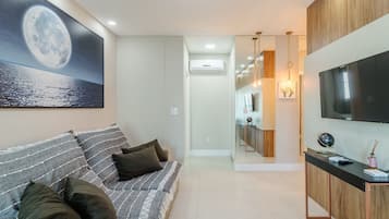 A modern living room with a large flat-screen TV, a sofa with cushions, and a painting of a moon on the wall.
