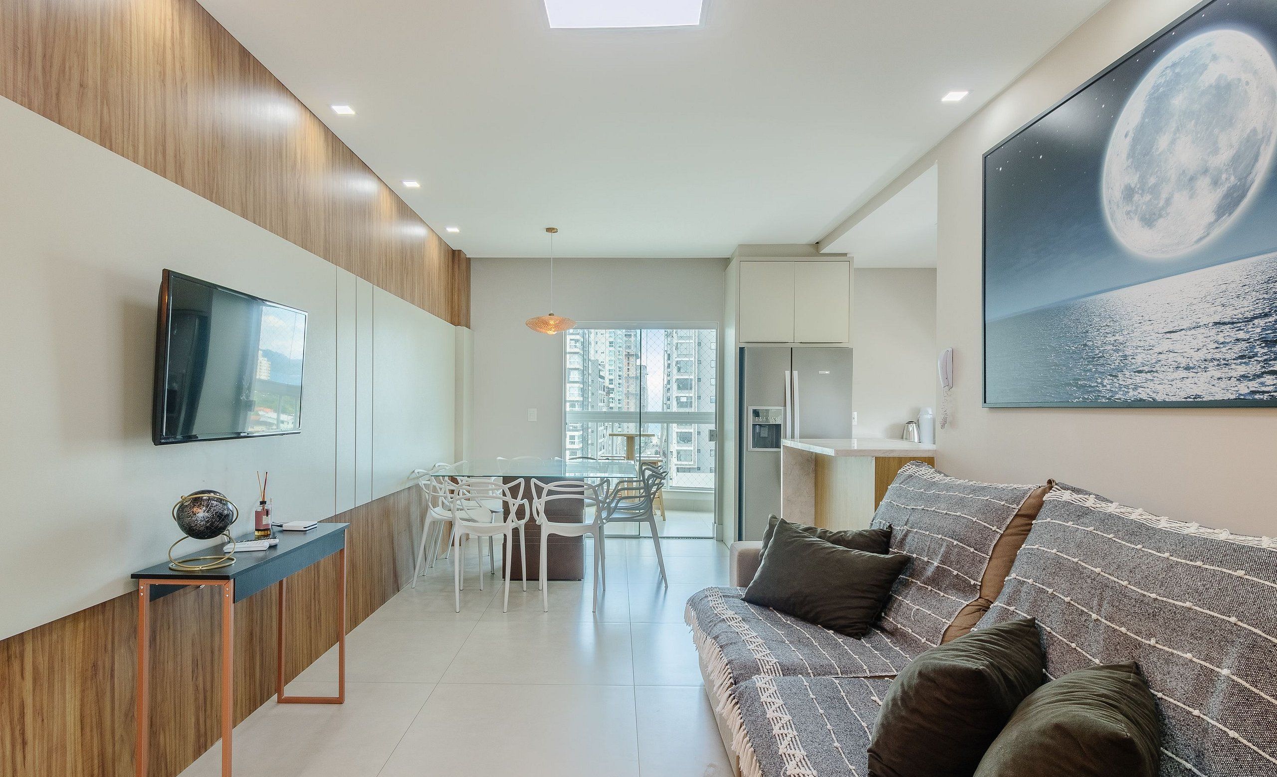 Un espacio moderno para vivir con sofá, televisión en la pared, mesa de comedor con sillas y zona de cocina con refrigerador.