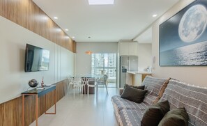 A modern living area with a sofa, a TV mounted on the wall, a dining table with chairs, and a kitchen area with a refrigerator. - 3 Suite ap 600 m From the Beach Porto Belo Pdp904 (Porto Belo)