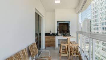 A balcony with wicker chairs, a small wooden table, and a kitchen area with a black countertop and wooden cabinets.
