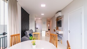 En moderne stue med spiseplads, med et rundt bord, træstole, en grå sofa og en væg med sorte mursten.