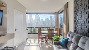 En moderne stue med en grå sofa, et spisebord med stole og et stort vindue med udsigt over byen.