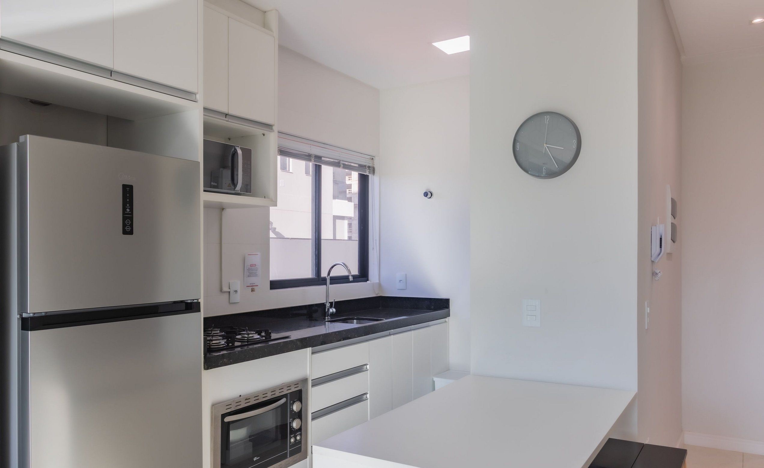 Una cocina moderna con armarios blancos, un refrigerador de acero inoxidable, horno empotrado y encimera negra.