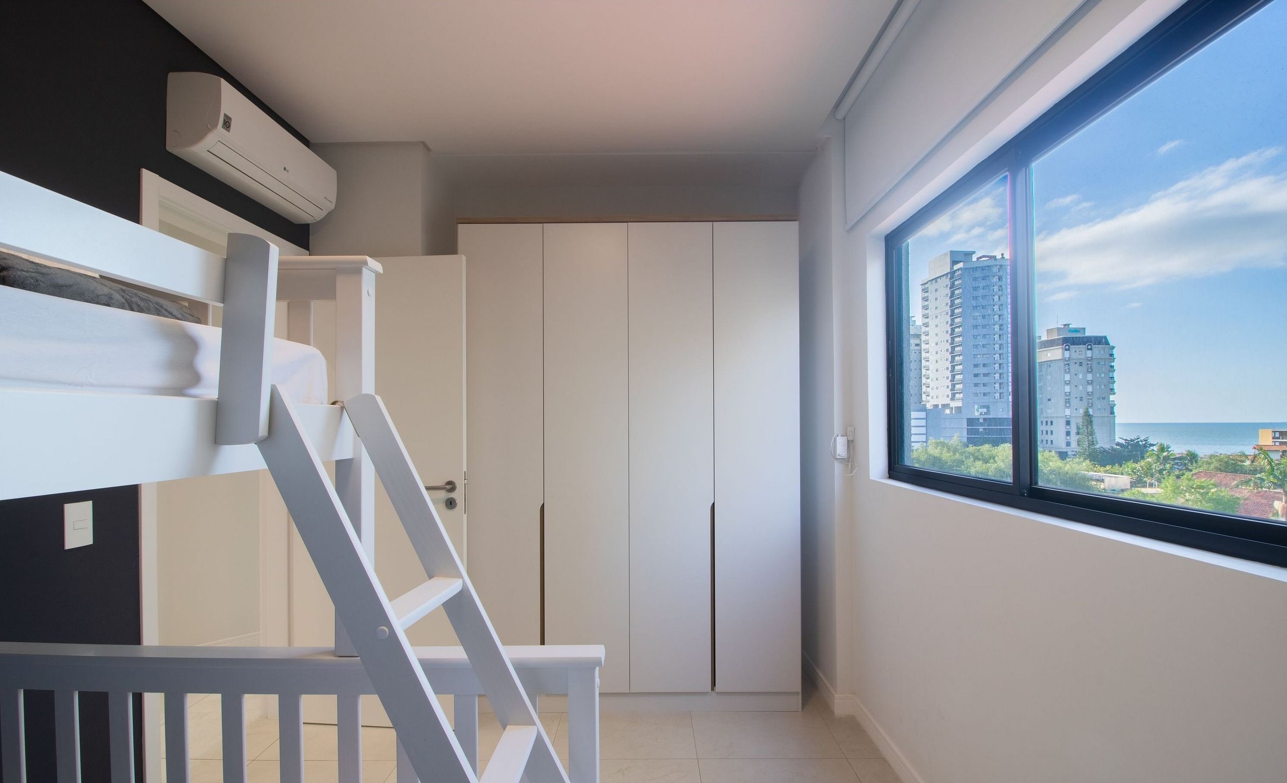 Un dormitorio con una litera, un armario y un ventanal con vistas a la ciudad.