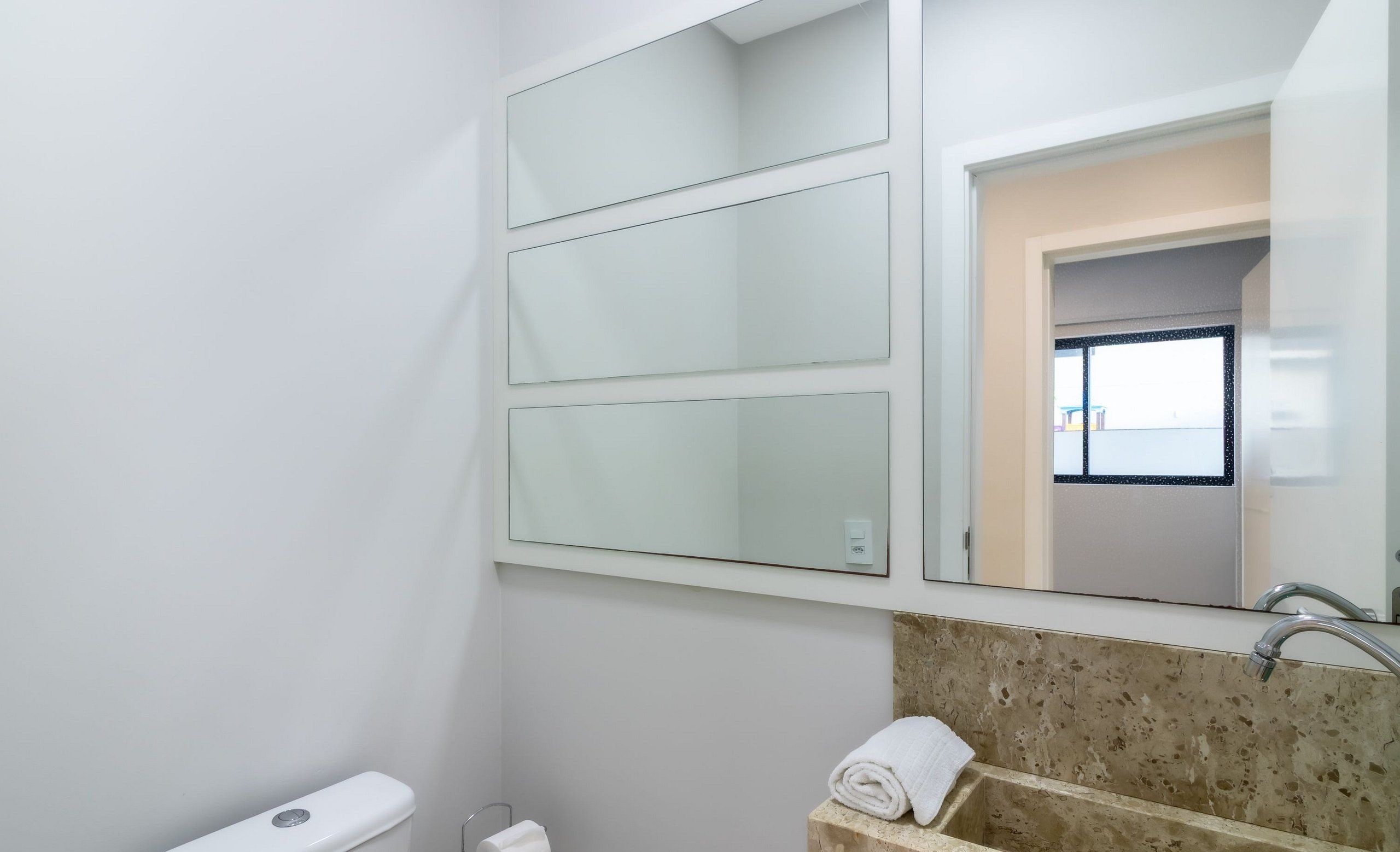 Ein Badezimmer mit Toilette, Waschbecken mit Marmorplatte und drei Spiegeln.