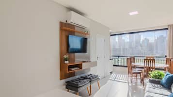 A modern living room with a flat-screen TV, a sofa, a bench, and a balcony with a dining area.