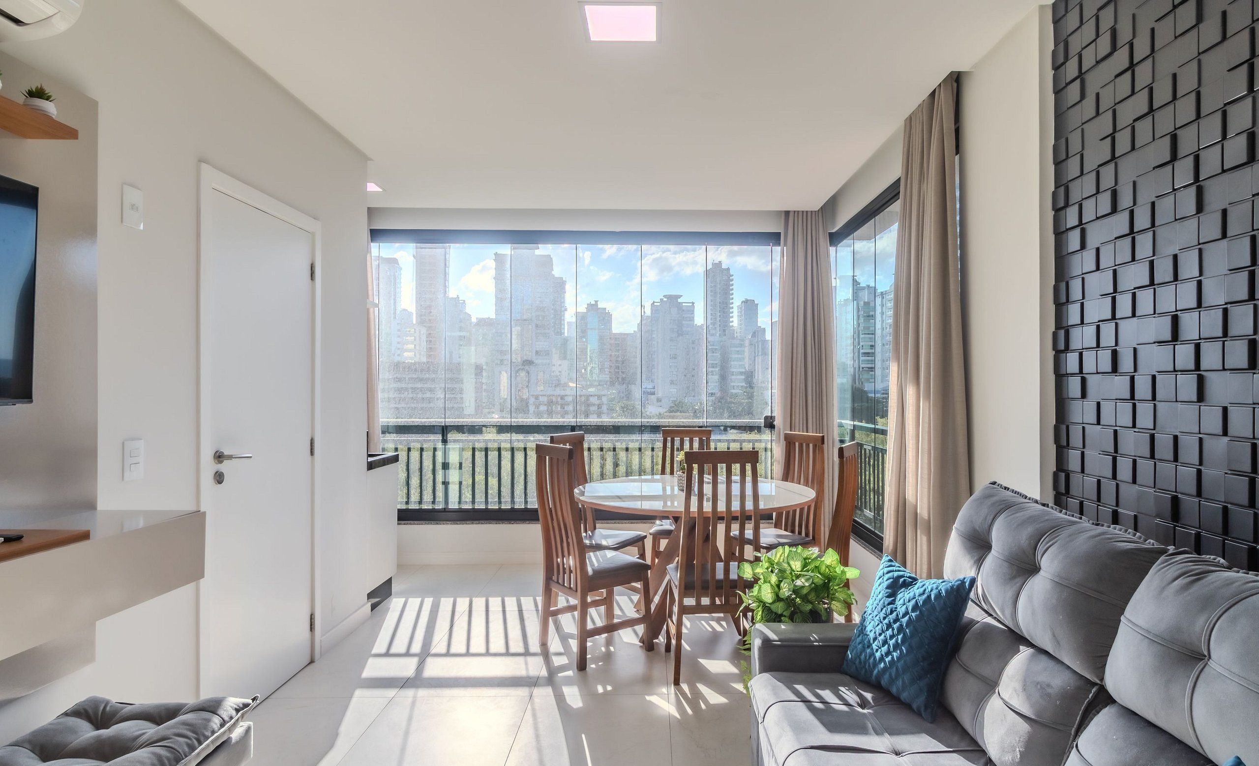 A modern living room with a grey sofa, a dining table with chairs, and a large window with a city view.