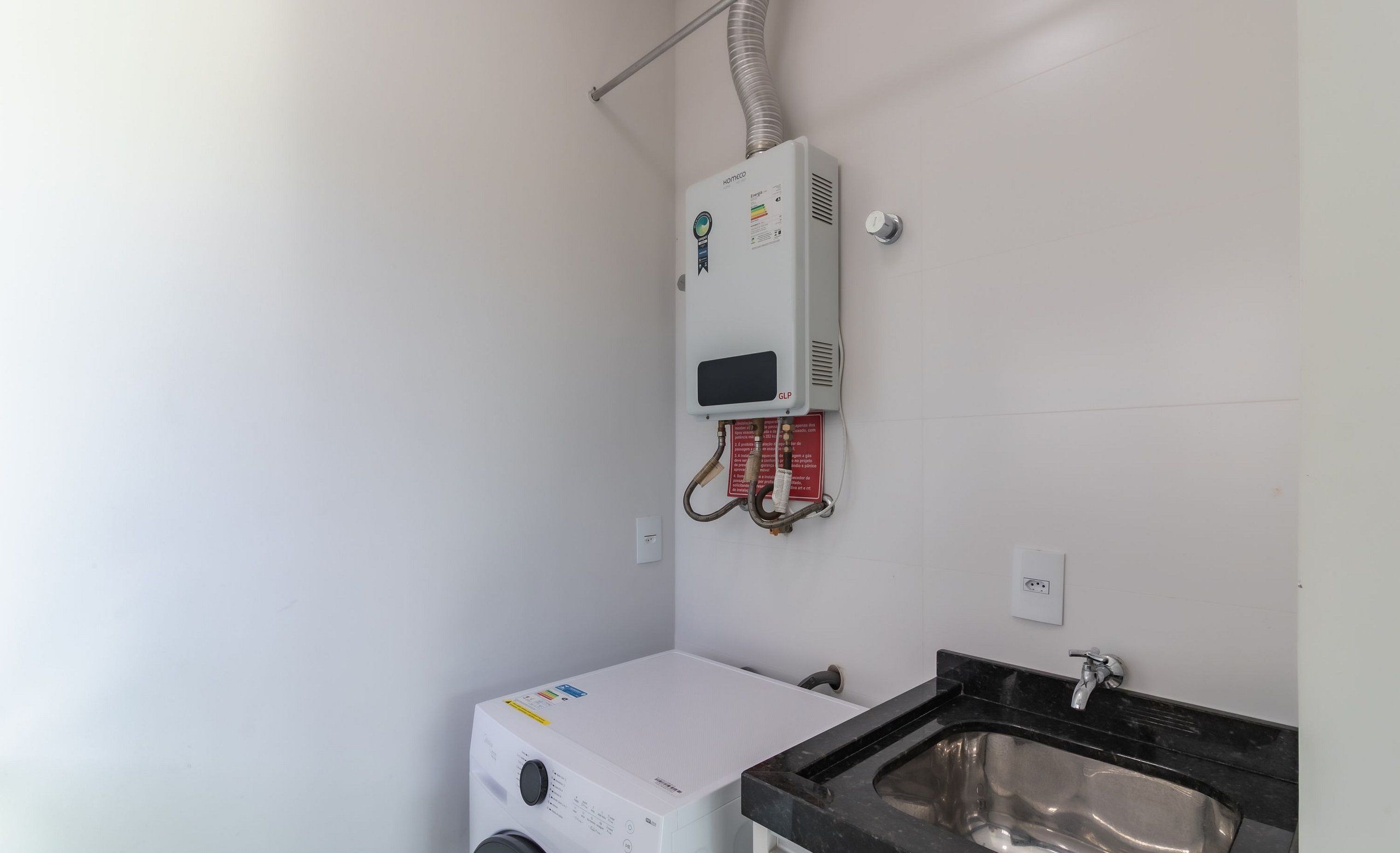 A compact bathroom with a washing machine, a sink, and a heater mounted on the wall.