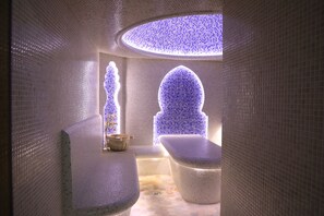 A modern bathroom with mosaic tile walls, a freestanding bathtub, and a large arched window. - Mubina Hotel (Bukhara)