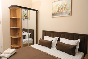 A neatly made bed with brown and white bedding, a wooden wardrobe with a mirror, and a framed floral painting on the wall. - Mubina Hotel (Bukhara)
