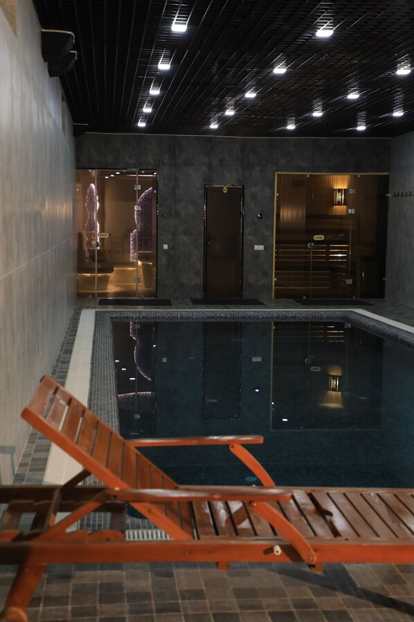 A swimming pool with a wooden lounge chair in the foreground, a shower area, and a door leading to another room. - Mubina Hotel (Bukhara)