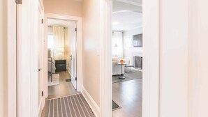 A hallway leading to a bedroom with a bed, nightstand, and lamp.