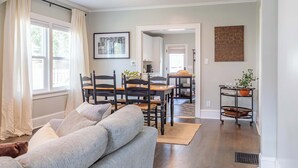 A living room with a sofa, dining table, chairs, and a kitchen area in the background.