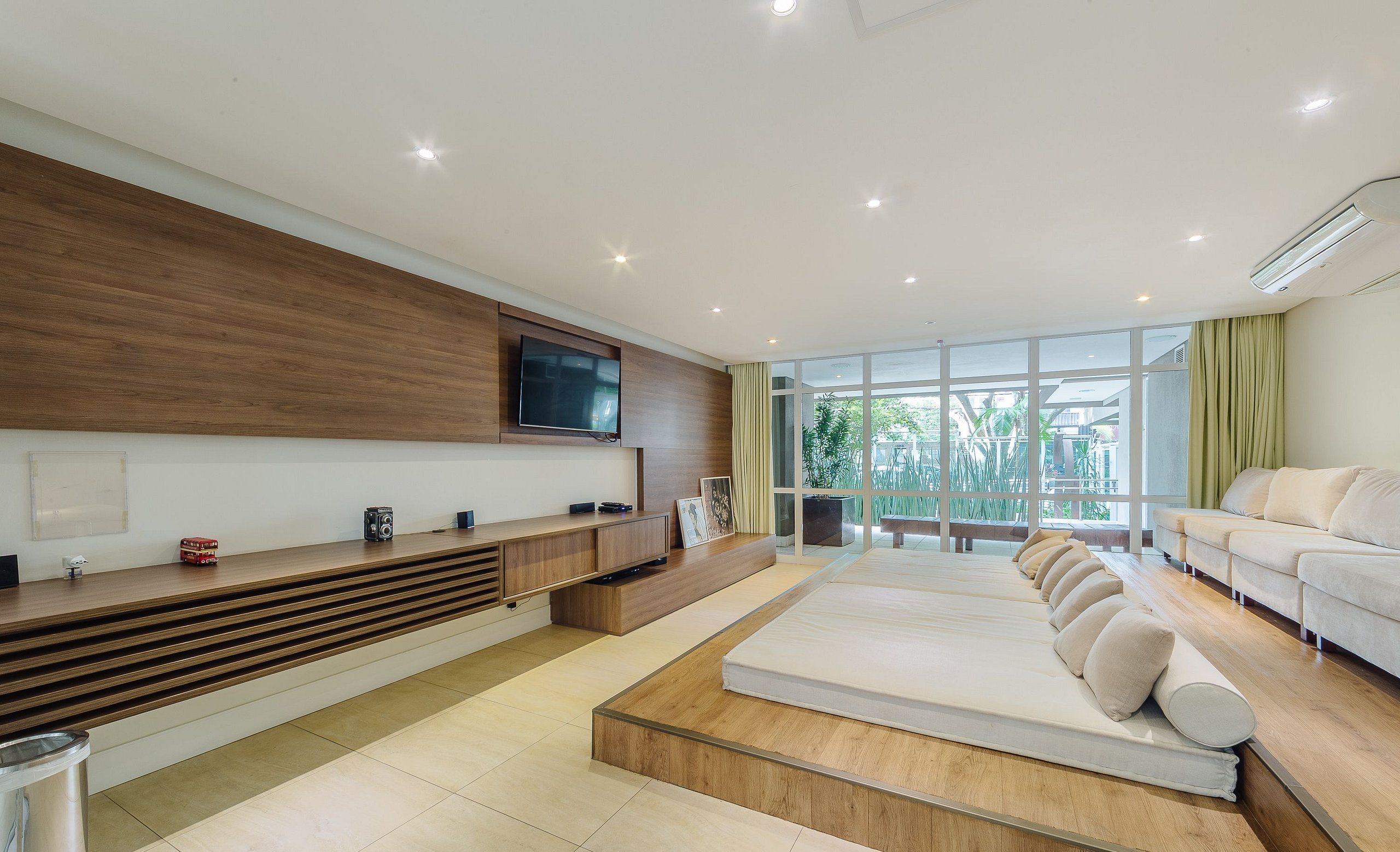 A modern bedroom with a large bed, a TV mounted on the wall, and a view of the outdoors.