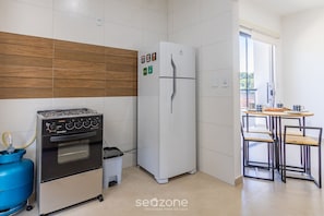 Une cuisine compacte équipée d’une cuisinière à gaz, d’un four, d’un réfrigérateur blanc et d’un petit coin repas avec une table et des chaises.
