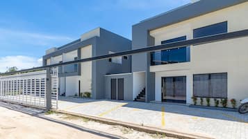 A modern two-story residential building with a flat roof, large windows, and a covered outdoor area with a metal fence.